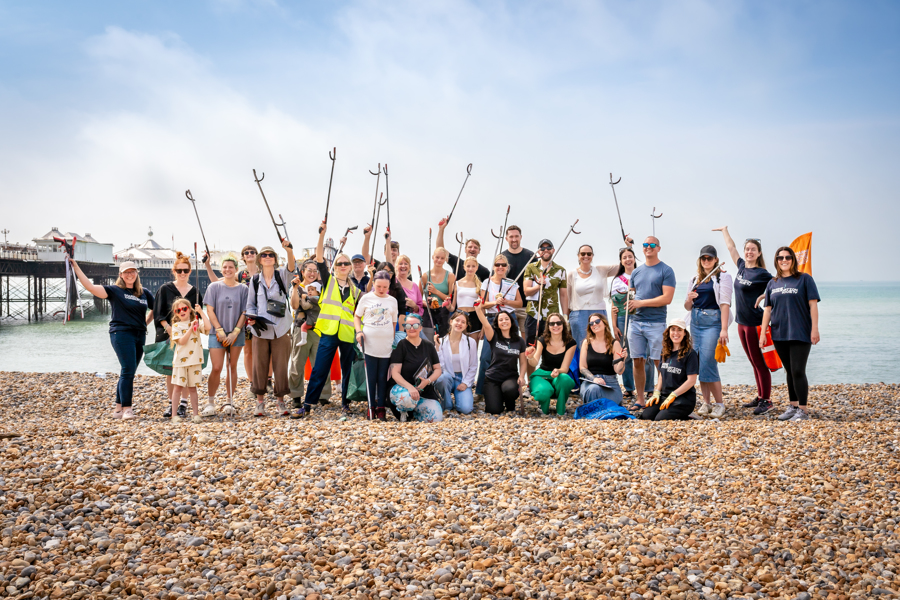 A group of volunteers stand on Brighton beach holding up their litter-pickers.
